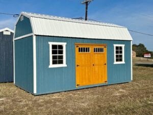 Front exterior view of a blue lofted barn-style portable shed with white trim, yellow double doors, and two front windows
