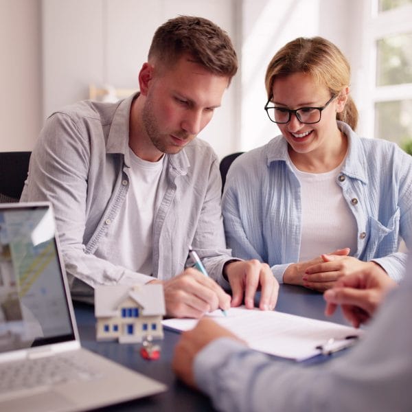 Happy Hispanic Real Estate Agent Shows House to Young Latinx Couple on Laptop at Office Desk for Mortgage Consultation.